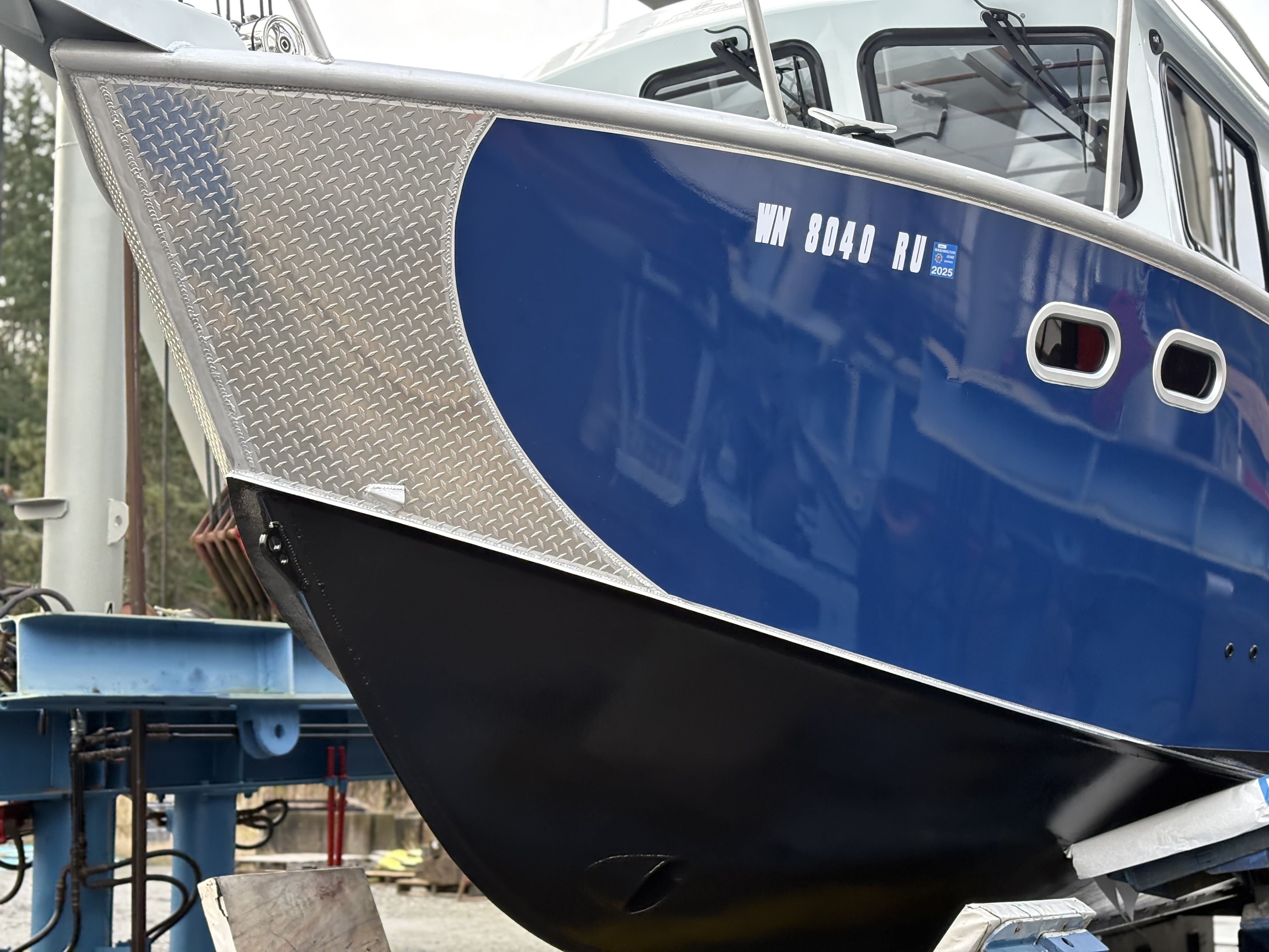 The bow of an aluminum pilothouse workboat lifted clear on the hard at Essential Shipyard
