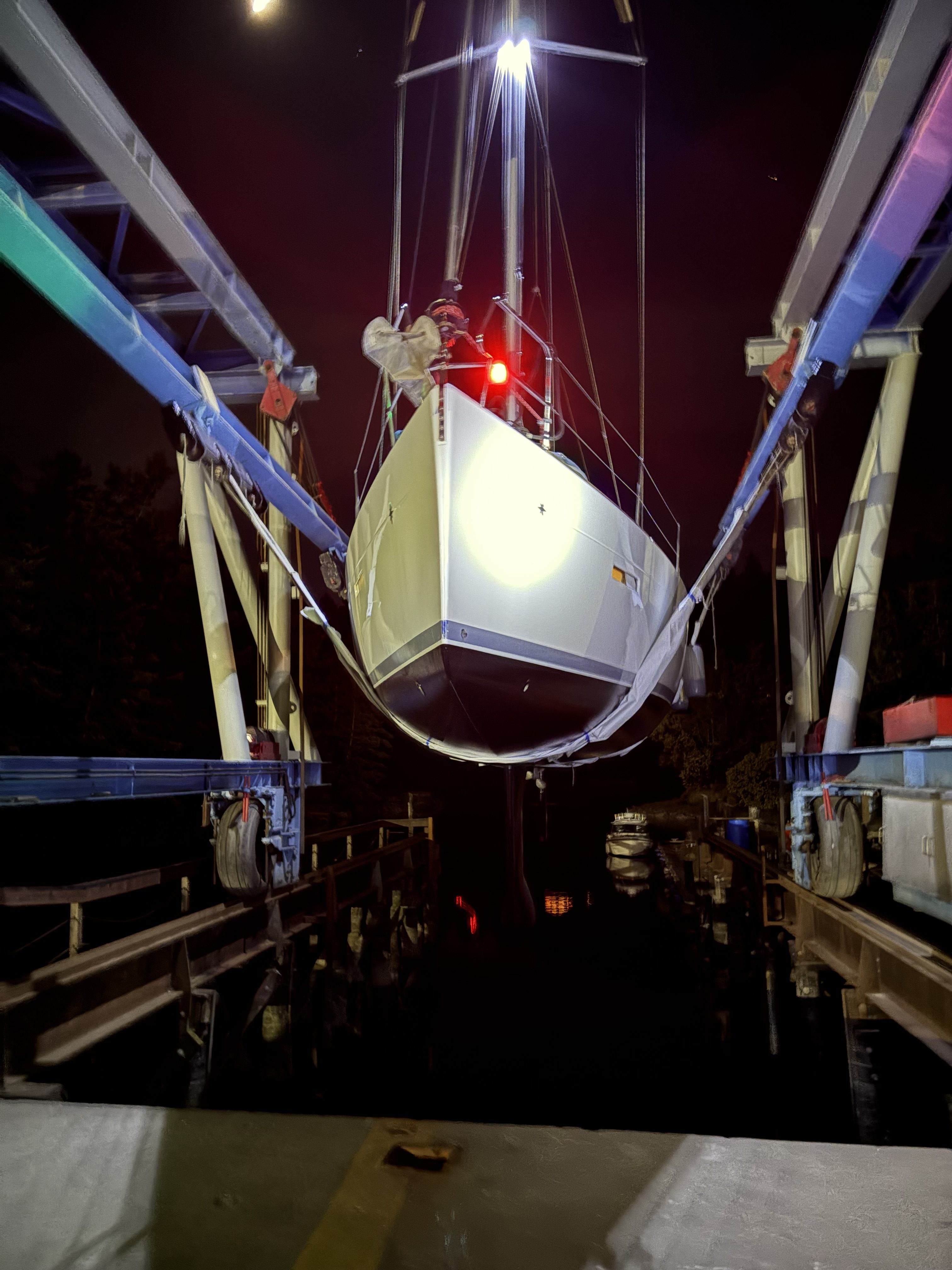 Sailboat lifted in the travel lift slings at night under work lights at Essential Shipyard, La Conner