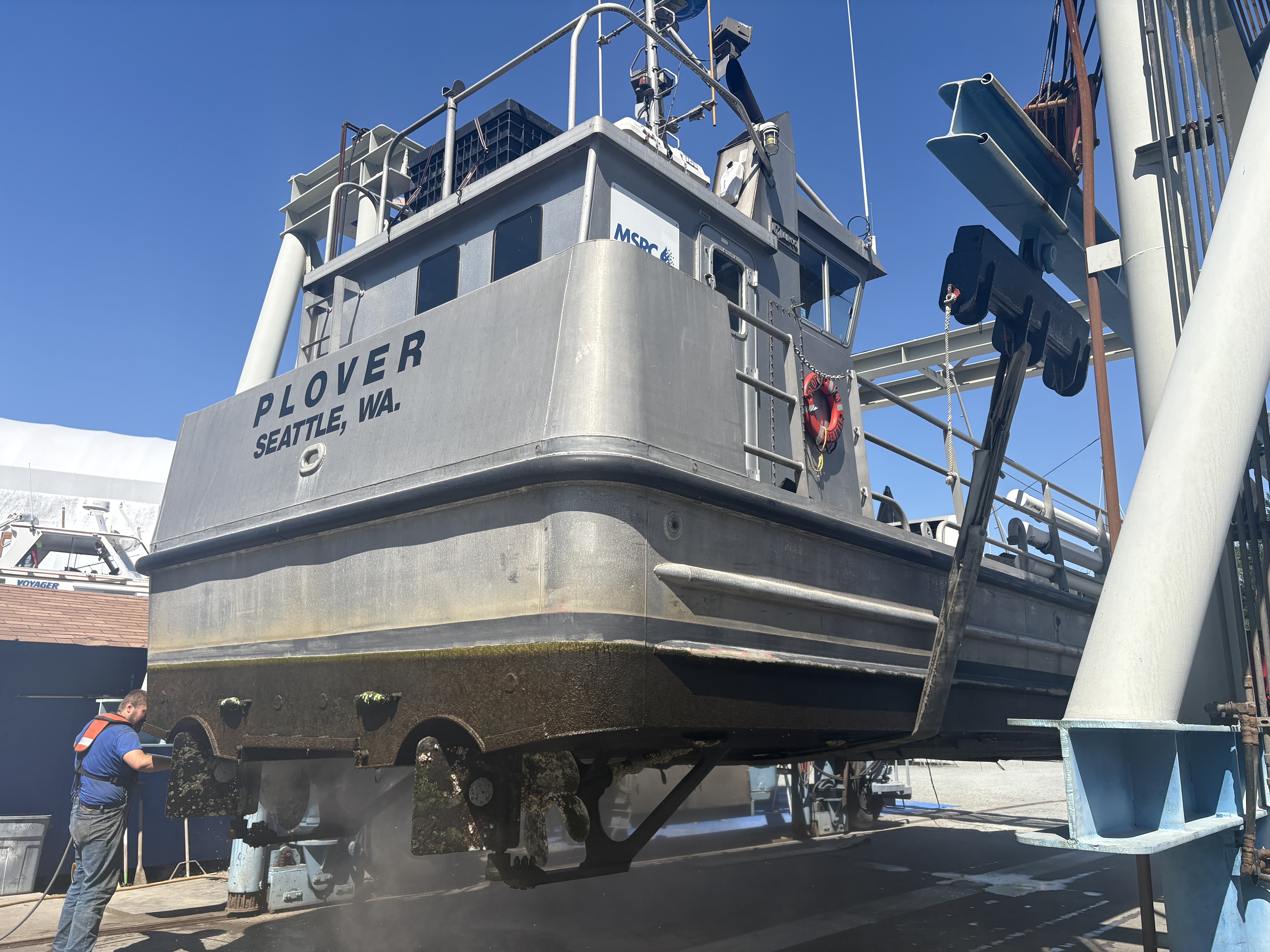 An aluminum commercial fishing vessel lifted in the travel lift slings at Essential Shipyard, Anacortes
