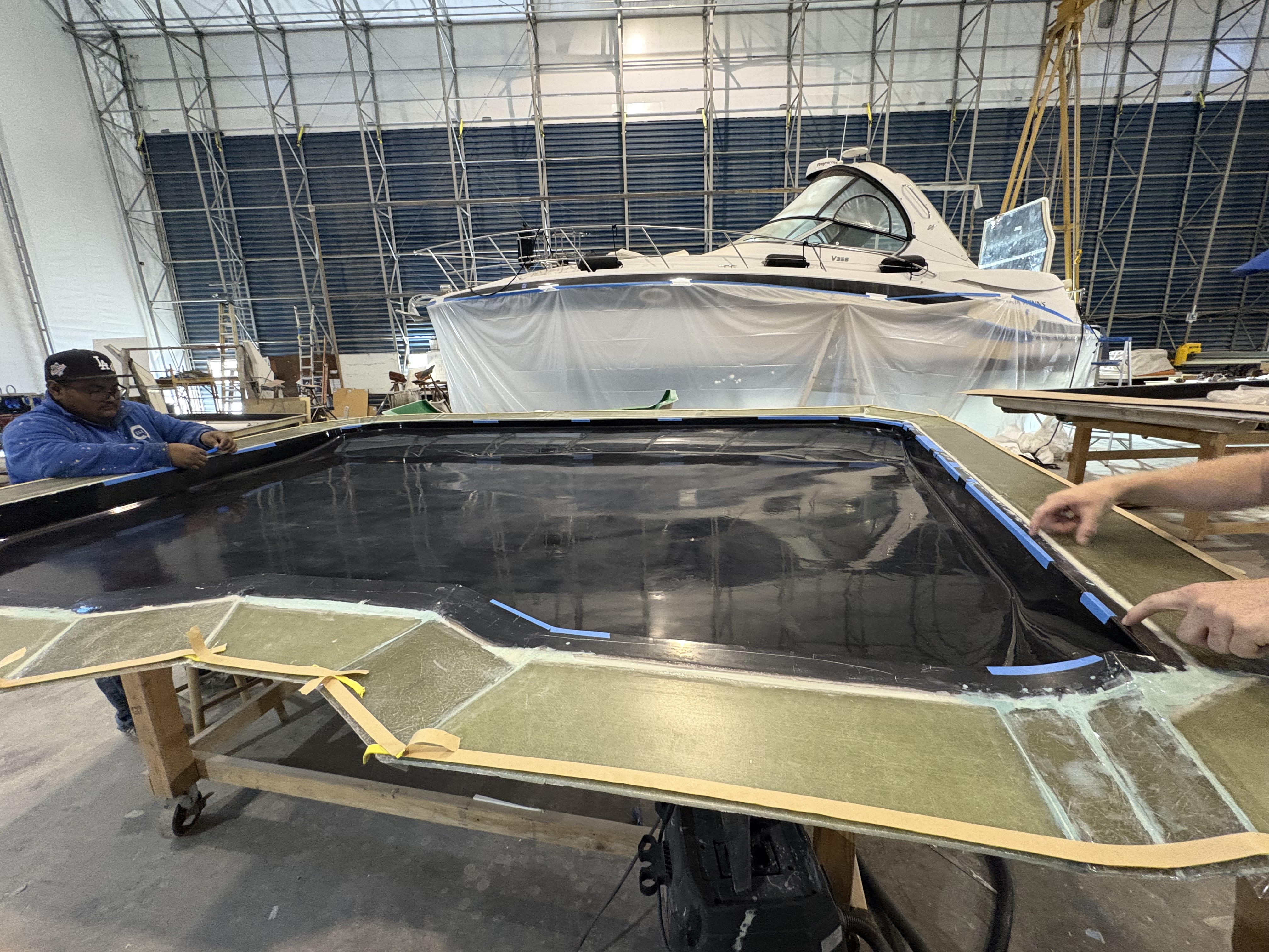 Laminated part on the layup table, boat in build behind, Essential Shipyard