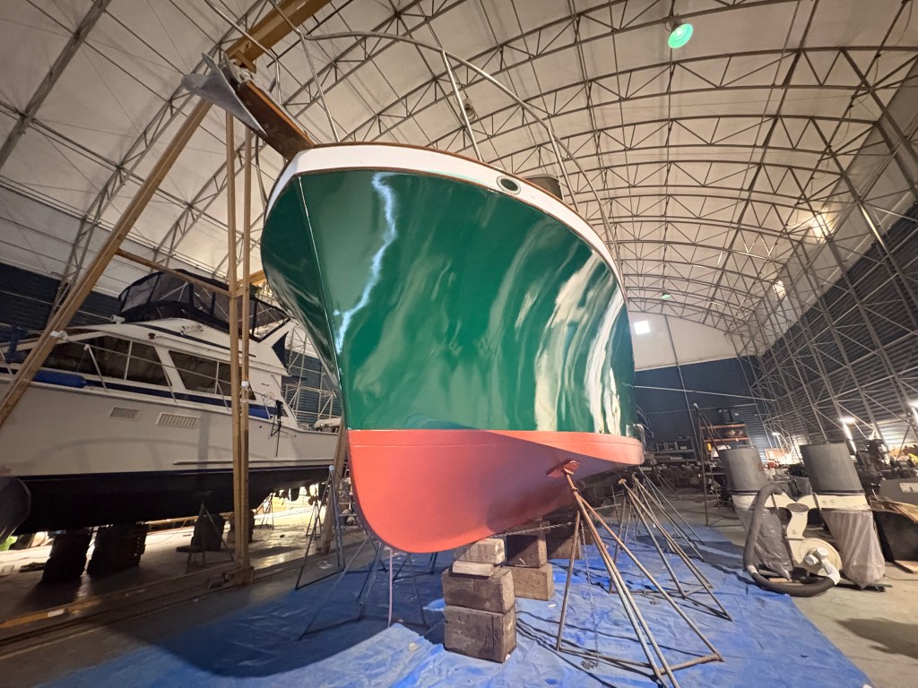 Large trawler with a deep green painted hull and red bottom, finished and blocked in the covered yard at Essential Shipyard